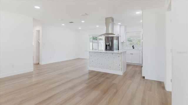 kitchen featuring stainless steel fridge, island range hood, white cabinetry, light wood-type flooring, and light countertops