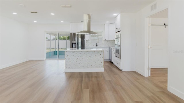 kitchen with island range hood, baseboards, light wood-style floors, multiple ovens, and stainless steel fridge