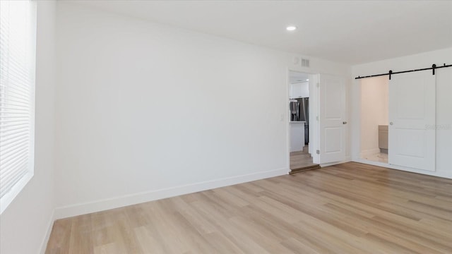unfurnished bedroom featuring a barn door, light wood-type flooring, baseboards, recessed lighting, and stainless steel fridge