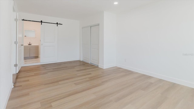 unfurnished bedroom with light wood-type flooring, a barn door, baseboards, a closet, and ensuite bathroom