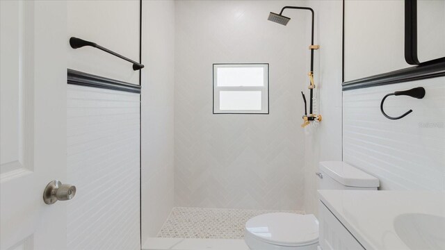 bathroom featuring a tile shower, toilet, and vanity
