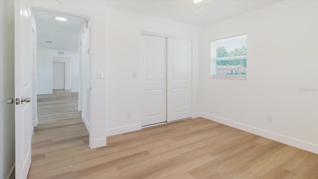 unfurnished bedroom featuring light wood-style flooring, baseboards, and a closet
