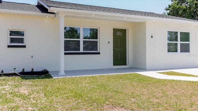 doorway to property featuring a yard, a shingled roof, and stucco siding