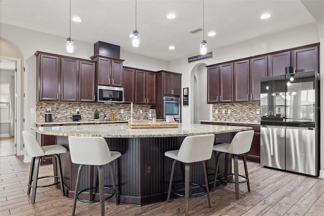 kitchen featuring stainless steel appliances, arched walkways, light wood-style flooring, decorative backsplash, and light stone countertops