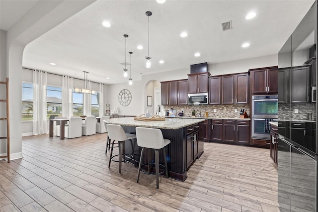 kitchen featuring stainless steel appliances, arched walkways, tasteful backsplash, recessed lighting, and a kitchen breakfast bar