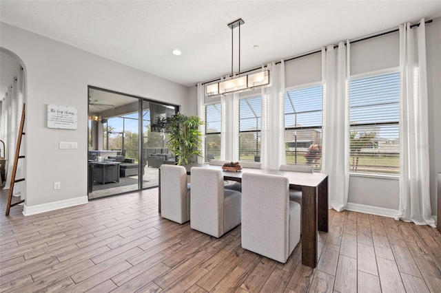 dining room with baseboards, wood finished floors, arched walkways, and recessed lighting