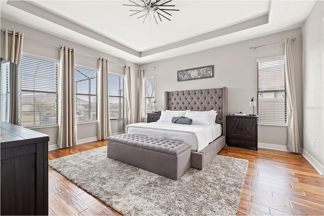 bedroom featuring a raised ceiling, multiple windows, and baseboards