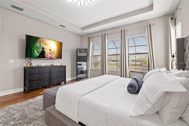 bedroom with wood finished floors, baseboards, and a raised ceiling