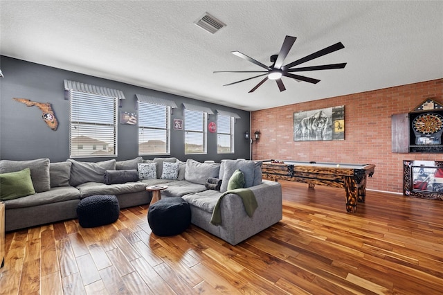 living room with ceiling fan, hardwood / wood-style flooring, a textured ceiling, brick wall, and billiards table