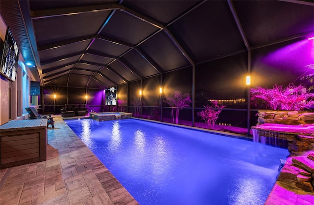 pool at twilight with a pool with connected hot tub, a patio, and glass enclosure