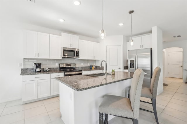 6398 Bar S Bar Trl, Zephyrhills, FL 33541 - kitchen featuring appliances with stainless steel finishes, a sink, arched walkways, dark stone counters, and light tile patterned flooring