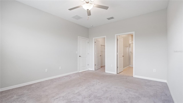 unfurnished bedroom with light colored carpet, a spacious closet, baseboards, ceiling fan, and ensuite bathroom