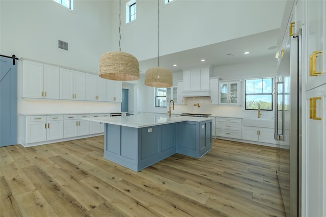 3515 Powerline Rd, Lithia, FL 33547 - kitchen featuring a towering ceiling, light wood finished floors, white cabinetry, light countertops, and an island with sink