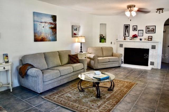 10170 W Yulee Dr, Homosassa, FL 34448 - living area featuring arched walkways, ceiling fan, a fireplace, and dark tile patterned flooring