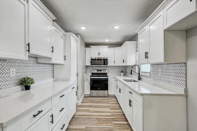 kitchen with appliances with stainless steel finishes, a sink, tasteful backsplash, white cabinetry, and recessed lighting