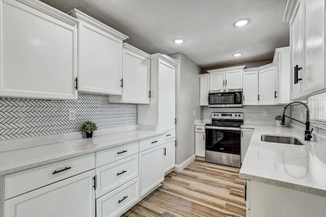 kitchen featuring appliances with stainless steel finishes, a sink, tasteful backsplash, white cabinets, and recessed lighting
