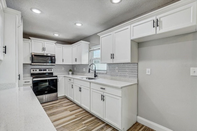 kitchen featuring stainless steel appliances, a sink, white cabinetry, tasteful backsplash, and a textured ceiling