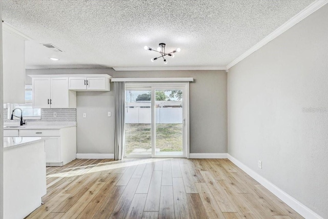unfurnished dining area featuring ornamental molding, light wood-style floors, baseboards, a sink, and a textured ceiling