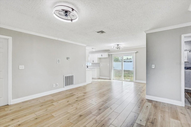 unfurnished living room with crown molding, a textured ceiling, light wood finished floors, baseboards, and a sink
