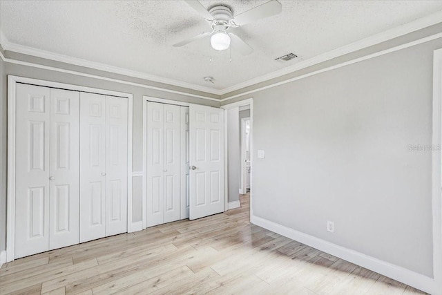 unfurnished bedroom featuring multiple closets, a textured ceiling, crown molding, baseboards, and wood finished floors