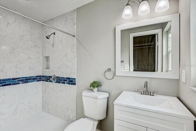 bathroom featuring toilet, a tile shower, and vanity