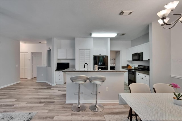 2220 Chianti Pl Unit 8-0828, Palm Harbor, FL 34683 - kitchen featuring black appliances, an island with sink, white cabinetry, dark countertops, and a breakfast bar