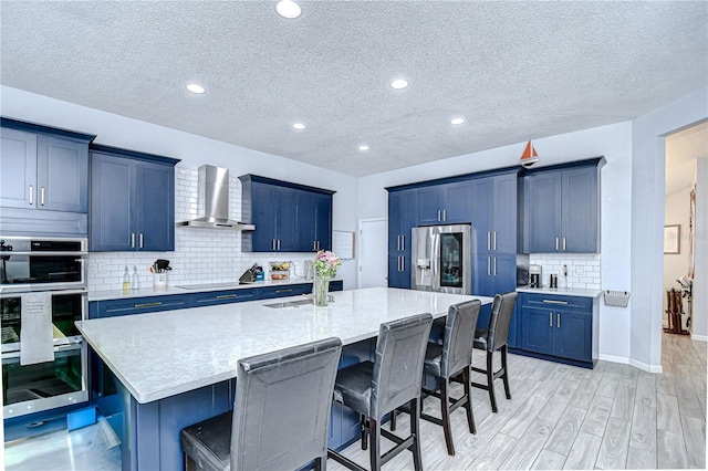 2020 Elk Spring Dr, Brandon, FL 33511 - kitchen with stainless steel fridge with ice dispenser, wall chimney range hood, blue cabinets, a kitchen bar, and a textured ceiling