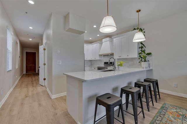 330 Lang Ct N Unit 1, Saint Petersburg, FL 33701 - kitchen featuring premium range hood, light wood-style floors, light countertops, a peninsula, and a breakfast bar