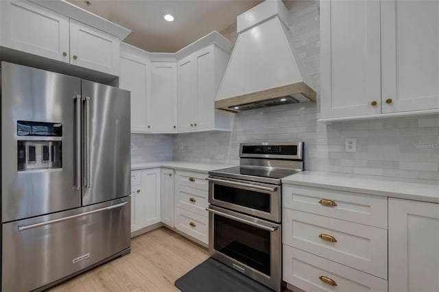 330 Lang Ct N Unit 1, Saint Petersburg, FL 33701 - kitchen featuring appliances with stainless steel finishes, custom range hood, white cabinets, light wood-style floors, and backsplash