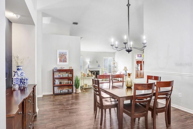 dining space featuring dark wood finished floors, a chandelier, baseboards, and a fireplace