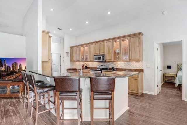 kitchen featuring stainless steel appliances, a kitchen bar, wood finished floors, glass insert cabinets, and decorative backsplash