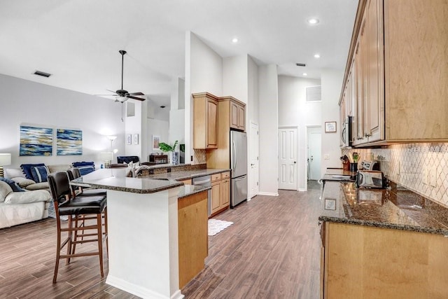 kitchen with stainless steel appliances, open floor plan, a high ceiling, a kitchen breakfast bar, and a peninsula