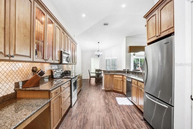 kitchen featuring appliances with stainless steel finishes, vaulted ceiling, glass insert cabinets, decorative backsplash, and a peninsula