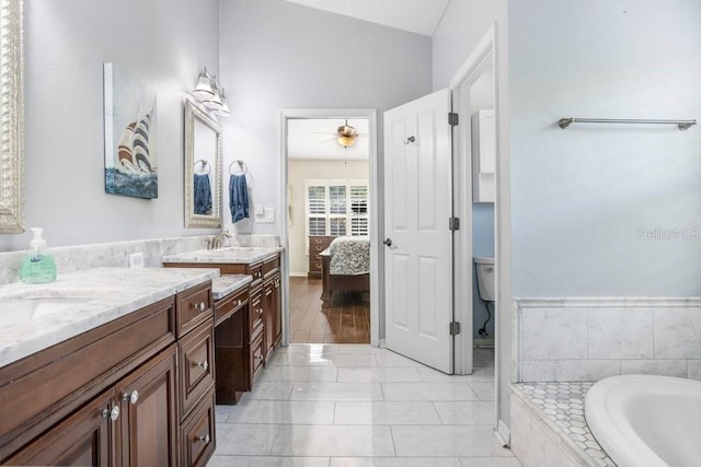 ensuite bathroom with vanity, toilet, a ceiling fan, tiled tub, and tile patterned floors