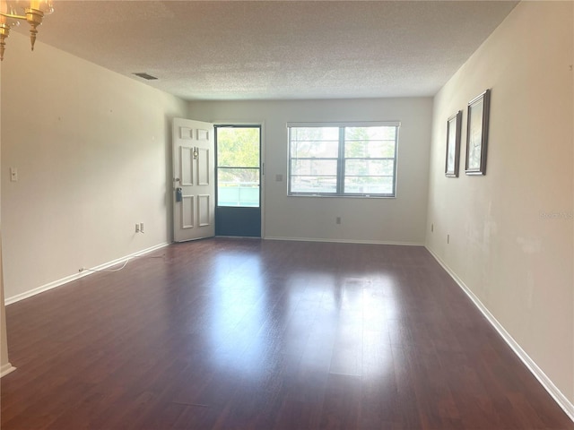 unfurnished room featuring a textured ceiling, dark wood finished floors, and baseboards