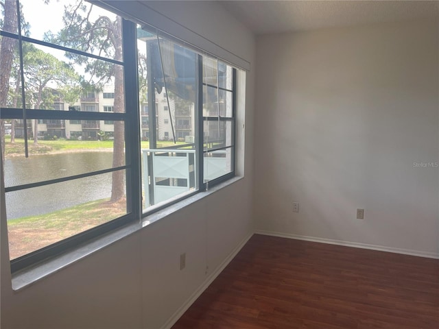 unfurnished room featuring wood finished floors, baseboards, and a water view