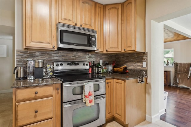 2814 W Humphrey St, Tampa, FL 33614 - kitchen with appliances with stainless steel finishes, dark stone countertops, backsplash, light wood-type flooring, and baseboards