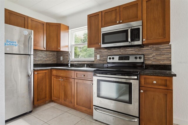 2814 W Humphrey St, Tampa, FL 33614 - kitchen with stainless steel appliances, a sink, backsplash, light tile patterned floors, and brown cabinets