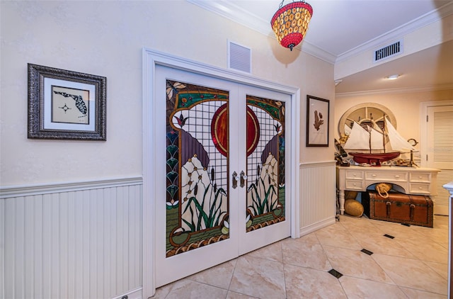 entrance foyer featuring ornamental molding, tile patterned floors, a wainscoted wall, french doors, and a decorative wall