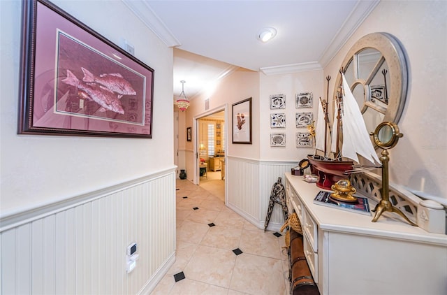 hall featuring crown molding, light tile patterned flooring, and a wainscoted wall