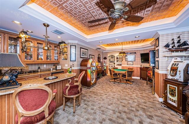 indoor wet bar featuring a tray ceiling, ornamental molding, ceiling fan, hanging light fixtures, and wainscoting
