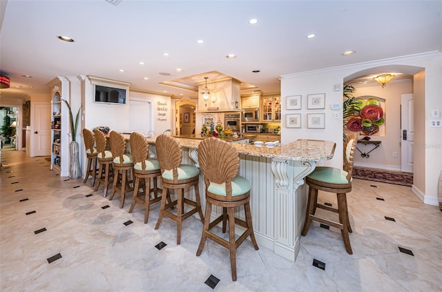 kitchen with ornamental molding, arched walkways, recessed lighting, a kitchen breakfast bar, and light stone counters