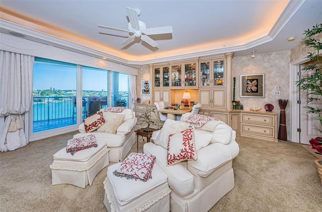 living area featuring a raised ceiling, carpet flooring, and a ceiling fan