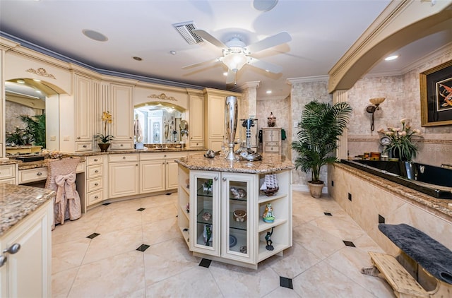 kitchen featuring cream cabinetry, light stone countertops, ornamental molding, glass insert cabinets, and ceiling fan
