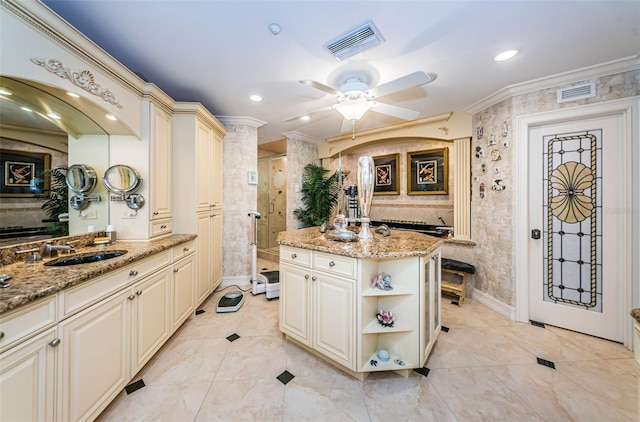 kitchen with cream cabinets, a sink, ornamental molding, a ceiling fan, and light stone countertops