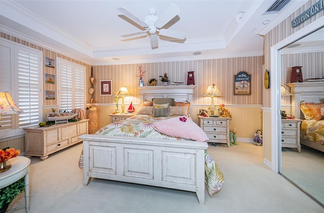 bedroom with light carpet, crown molding, a tray ceiling, ceiling fan, and a wainscoted wall