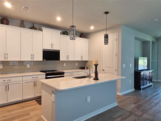 3776 Maxwell Park Dr, Sun City Center, FL 33573 - kitchen with stainless steel range with electric cooktop, a sink, light wood finished floors, decorative backsplash, and white cabinetry