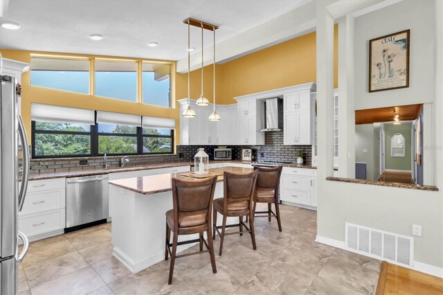 2287 Demaret Dr, Dunedin, FL 34698 - kitchen featuring appliances with stainless steel finishes, wall chimney range hood, a kitchen island, decorative backsplash, and a breakfast bar area
