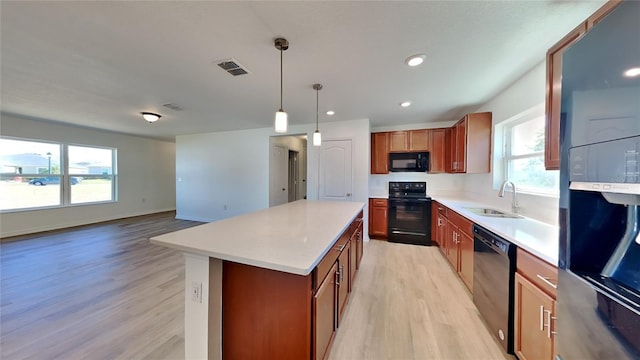 kitchen featuring black appliances, a sink, light wood-style floors, brown cabinetry, and a center island