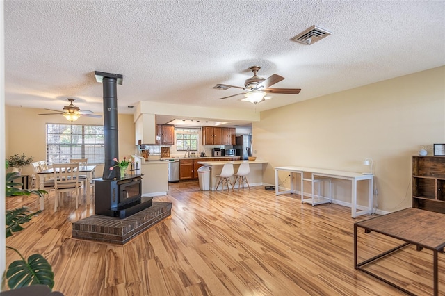 living room with a wood stove, ceiling fan, light wood finished floors, a textured ceiling, and baseboards